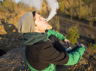 The young beautiful boy vaper against the sunset