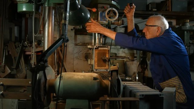 Tracking sequence of man drilling through metal with an old fashioned drilling machine in his workshop.
