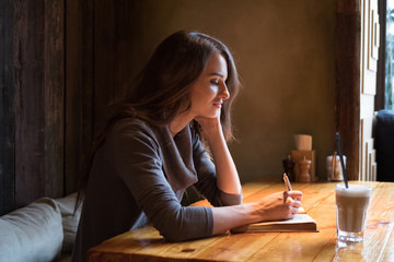 A woman sitting at a table in a cafe and making notes in diary a
