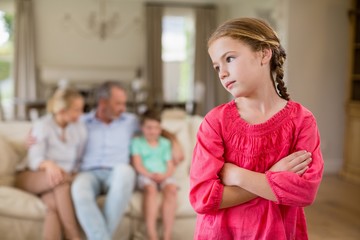 Thoughtful girl standing with arm crossed in living room