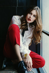 Naklejka premium Indoor full body portrait of young fashionable woman posing in loft interior. Model looking at camera. Lady wearing stylish clothes, watch, shoes. Female fashion concept. City lifestyle. 