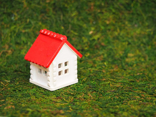 Toy house on a green grass background. Model of a small white house with a red roof