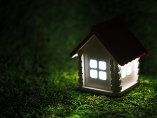 Toy house with luminous windows in the dark. Model little white home with a red roof at night