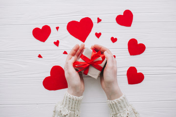 valentines day.female holding present  on white wooden background with  red hearts