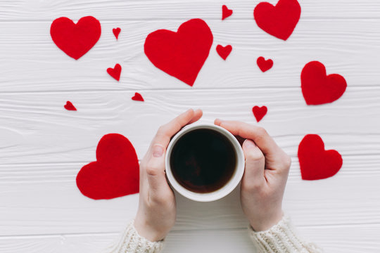 valentines day.female holding tee cup  on white wooden background with  red hearts