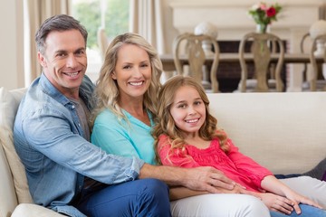 Portrait of parents and daughter sitting on sofa in living room