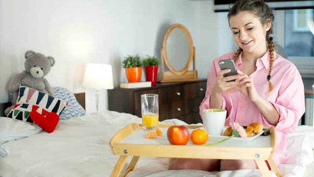 Happy girl in pyjamas doing photo of breakfast on smartphone and shares on her social medias

