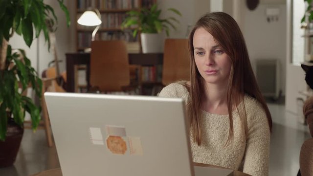 Young woman watches videos on internet in her laptop at home. She watches very concentrated and disgusted. She denies shaking her head. Dolly shot to the right.