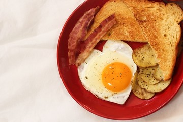 Valentine breakfast with heart shaped egg bacon bread toast and roasted potatoes served in red plate