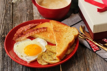 Breakfast for Valentine's day with Heart shaped egg bacon bread toast and cup of coffee served in a red plate