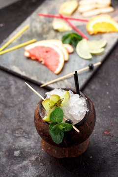Coconut with ice and fresh fruits (grapefruit, kiwi, orange ) and mint over concrete background.