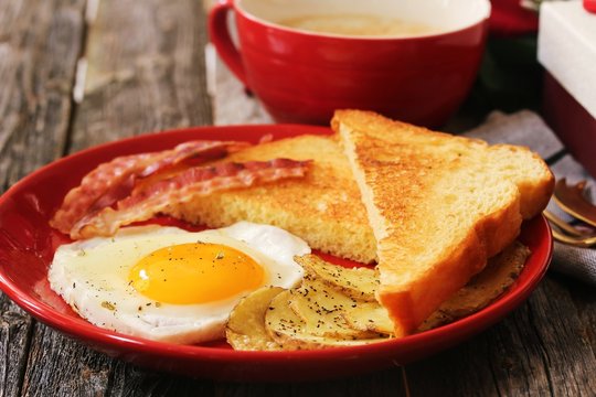 Breakfast For Valentine's Day With Heart Shaped Egg Bacon Bread Toast And Cup Of Coffee Served In A Red Plate