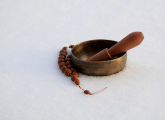 Tibetan singing bowl on a white snowy background and rosary.
