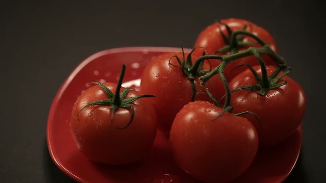 Close up refocusing shot of ripe fresh tomatoes branch lies on red plate on black table