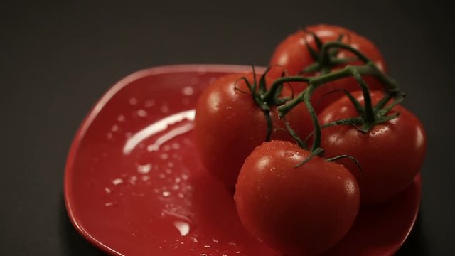 Close up shot of taking one ripe tomato from a red plate, and then put back. Plate on black table