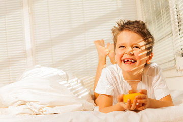 Obraz na płótnie Canvas Smiling boy laying in his bed with orange juice