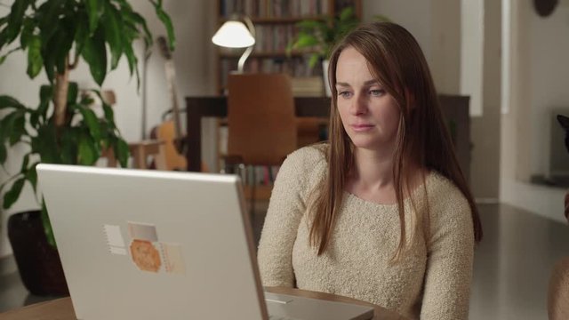Young woman watches videos on internet in her laptop at home. She watches very concentrated and serious with a suddenly look of disgust. Dolly shot to the right.