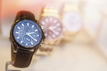 Beautiful black leather watch in front of other watches. Lens flare in background.