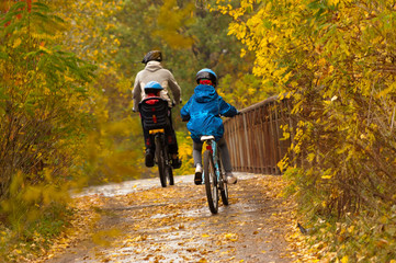 Family cycling outdoors, golden autumn in park
