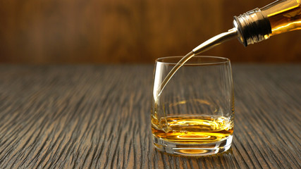 Pouring whiskey into the glass on a wooden table