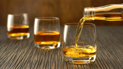 Pouring whiskey into the glass on a wooden table