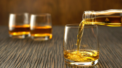 Pouring whiskey into the glass on a wooden table