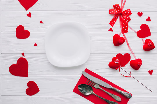 valentines day.plate ,cutlery ,knife,fork,red hearts on white wooden background 