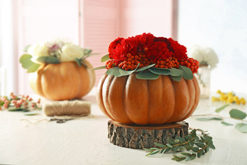 Beautiful composition of red flowers, berries and pumpkin on white table