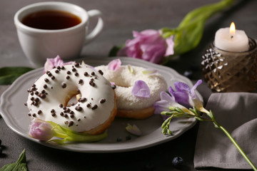 Delicious doughnuts, cup of coffee and flowers on grey table