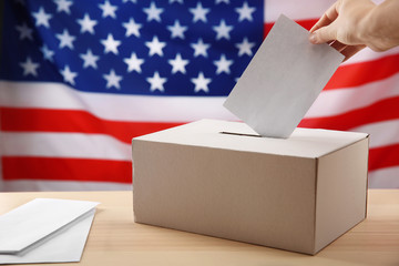 Hand inserting envelope in ballot box on USA national flag background