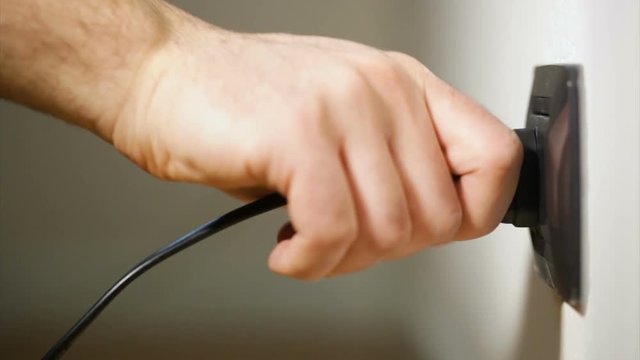 Hand detaches a plug from an electrical outlet.