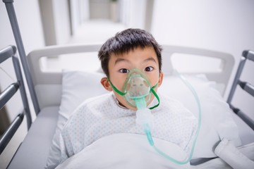 Boy patient wearing oxygen mask lying on hospital bed 