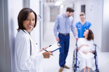 Portrait of smiling doctor holding clipboard in corridor