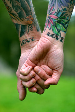A couple holding hands with LOVE tattooed on their wrists