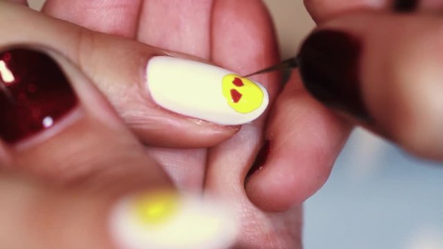 Manicure procedure woman hand drawing yellow emoji on white finger nail polish, close up