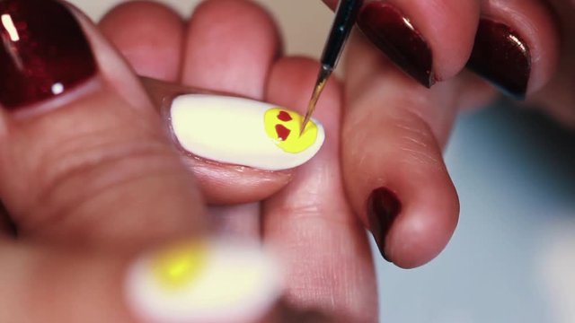 Manicure procedure female hand drawing yellow emoji on white finger nail polish, close up
