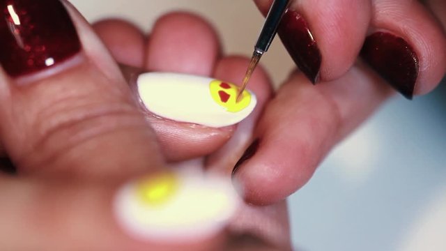 Manicure procedure female hand drawing yellow emoji on white finger nail polish, close up