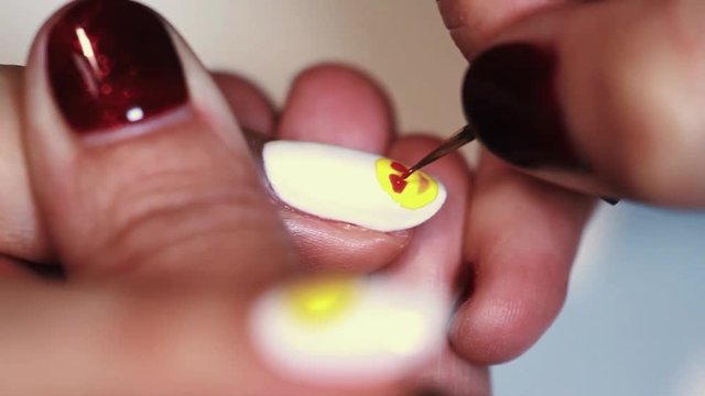 Manicure procedure female hand drawing yellow emoji on white finger nail varnish, close up