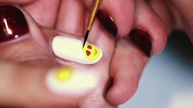 Manicure procedure woman hand drawing yellow emoji on white finger nail polish, close up