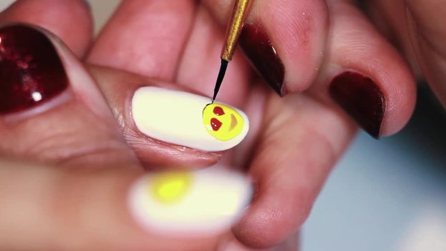 Manicure procedure woman hand painting yellow emoji on white finger nail polish, close up
