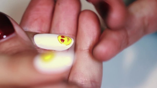 Manicure procedure woman hand painting yellow emoji on white finger nail varnish, close up