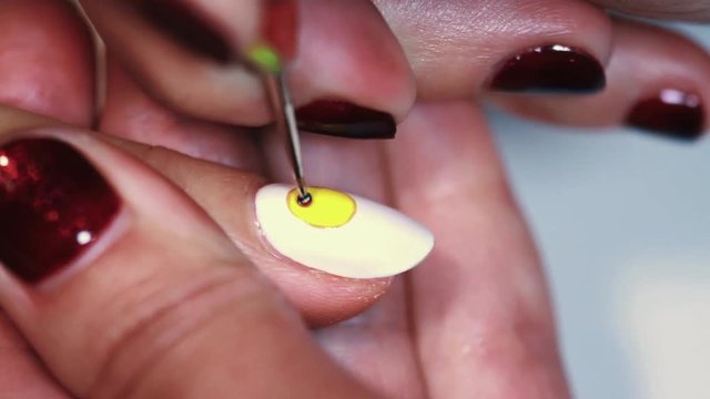 Manicure procedure female hand painting yellow emoji on white finger nail varnish, close up