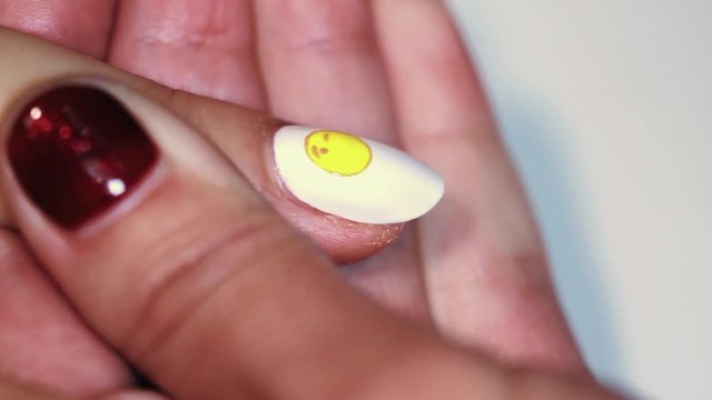 Manicure procedure female hand painting yellow emoji on white finger nail polish, close up
