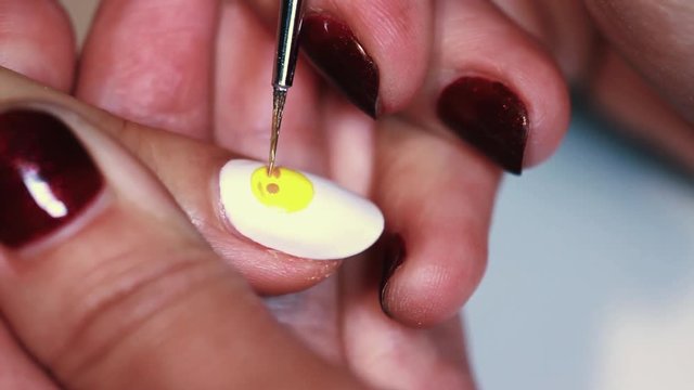 Manicure session female hand drawing yellow emoji on white finger nail polish, close up