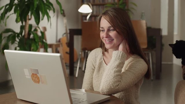 Young woman watches videos on internet in her laptop at home. She smiles and something surprised her.