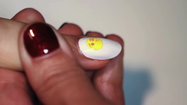 Manicure procedure woman hand paints yellow emoticon on white finger nail polish, close up