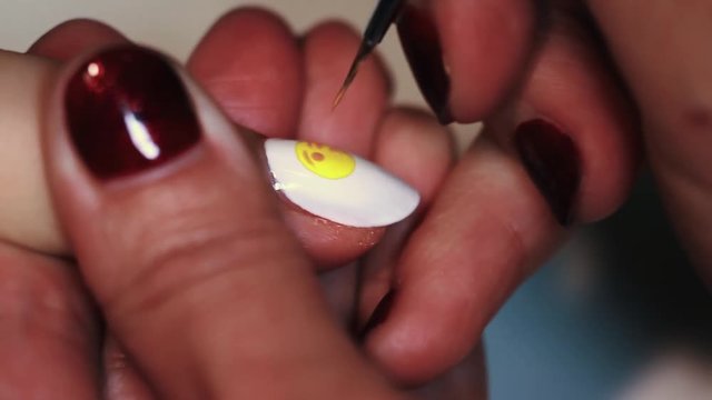 Manicure procedure woman hand paints yellow emoticon on white finger nail polish, close up