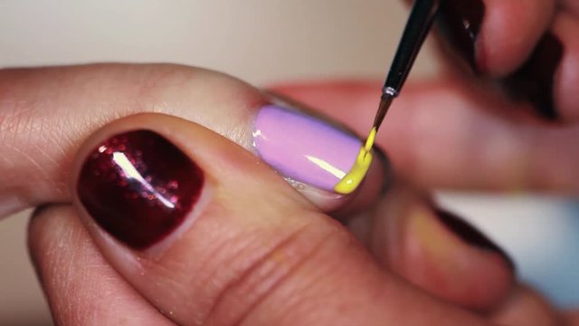 Manicure procedure woman hand drawing yellow stripe on purple finger nail polish, close up