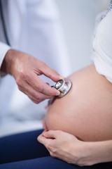 Fototapeta premium Doctor examining pregnant womans belly with stethoscope in ward