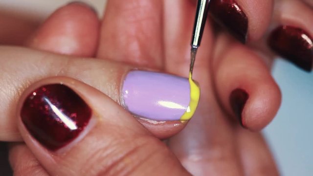 Manicure procedure female hand drawing yellow stripe on purple finger nail polish, close up